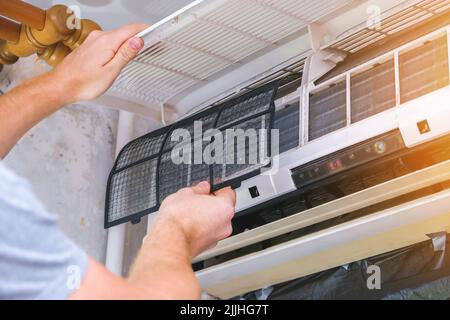 The man takes out filters from the air conditioner for cleaning. Split system maintenance. Stock Photo