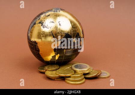 Global and business concept. On a brown surface is a miniature model of the world and coins. Stock Photo