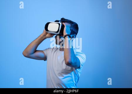 Bearded young man using VR glasses, touching with a hand copy space free space, playing virtual video games with friends online. Stock Photo