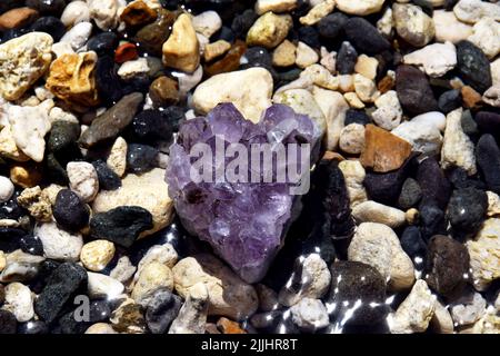 Beautiful purple amethyst crystals on wet pebbles on the seashore. Bright purple amethyst druse in the shape of a heart on the background of the sea. Stock Photo