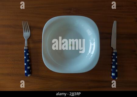 haute cuisine concept one pea on white plate with knife and fork on wood table Stock Photo