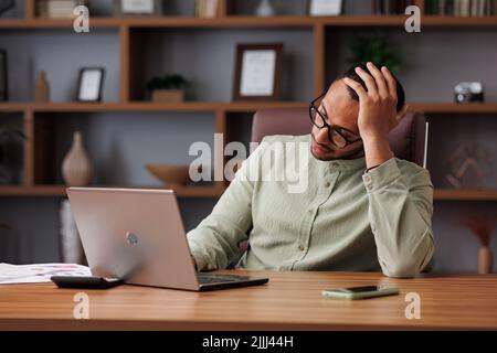 Depressed young man surprised by the bad news on laptop. Sad african american businessman feels frustrated about high bills, debt, tax invoice, credit Stock Photo