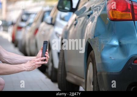 Stressed driver taking picture on sellphone camera of smashed vehicle calling for emergency service help after car accident. Road safety and insurance Stock Photo