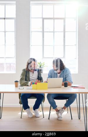 College students working together two young men brainstorming ideas for project sitting at desk using laptop computer in class Stock Photo