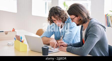 College students working together two young men brainstorming ideas for project sitting at desk using laptop computer in class Stock Photo