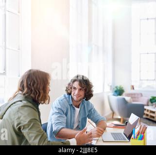 College students working together two young men brainstorming ideas for project sitting at desk using laptop computer in class Stock Photo