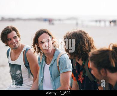 group of male friends on beach enjoying summer holiday students having fun on vacation attractive guys hanging out on beachfront at sunset Stock Photo