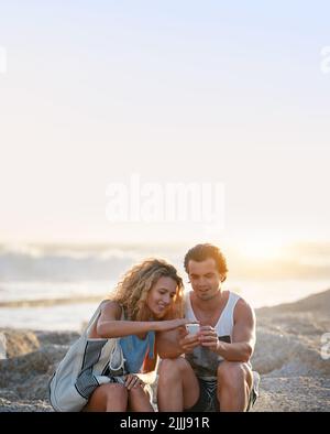 Young couple using smartphone on beach at sunset Stock Photo