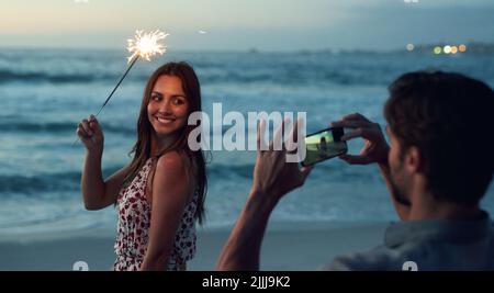 Beautiful woman holding sparkler posing for photo on romantic beach celebrating new years eve at sunset Stock Photo