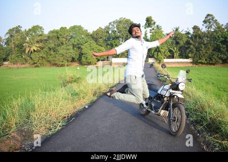 A man jumping and posing for photo with motorbike near paddy field Stock Photo