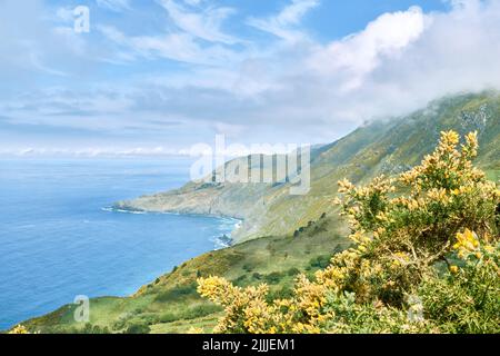 A nature scene of Vixia Herbeira green cliffs by water in Galicia under cloudy blue sky Stock Photo