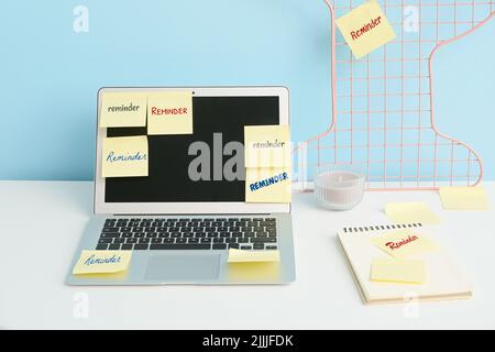 Laptop with sticky notes on table near blue wall Stock Photo