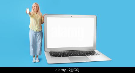Mature woman with smartphone and big laptop on blue background Stock Photo