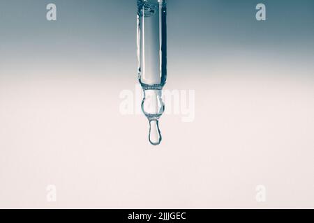 Liquid serum and dropper on a gradient background. Frontal view. Serum drops from a pipette. Stock Photo