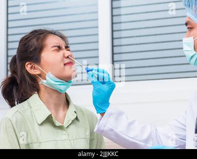 Coronavirus test, Doctor man take saliva sample through nose with cotton swab to check coronavirus test from Asian young woman, Covid-19 pandemic outb Stock Photo
