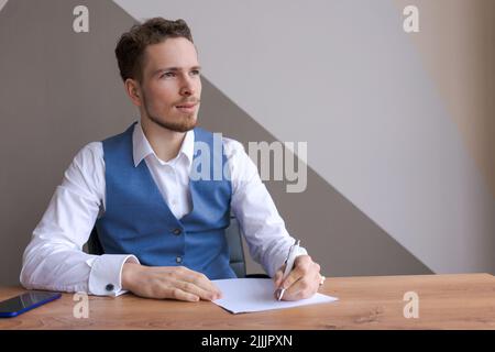 Young businessman with beard sits in office at table with documents and thinks about successful signing deal and the conclusion contract. Interview or discussion of plans for business development Stock Photo