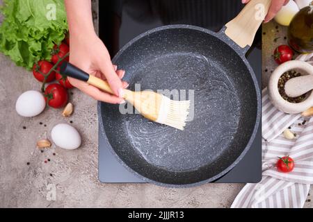 Woman smear olive oil on frying pan with silicone brush at domestic kitchen Stock Photo