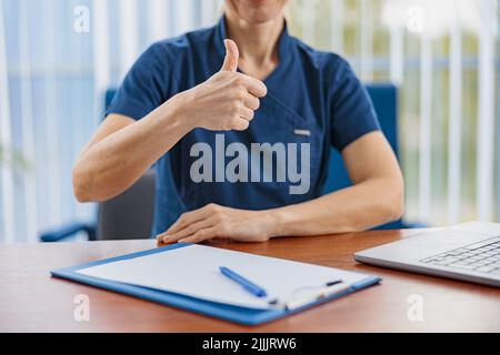 Close up of doctor working laptop and showing thumbs up in medical office  Stock Photo