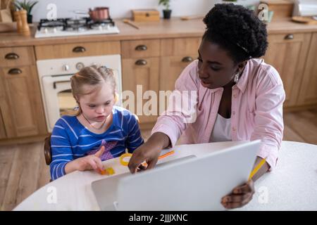 A girl with down syndrome having a lesson with her teacher and looking involved Stock Photo