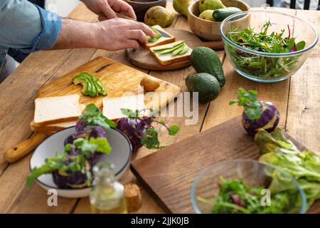 Man preparing avocado sandwiches at home kitchen Cooking a healthy and tasty breakfast or lunch Stock Photo