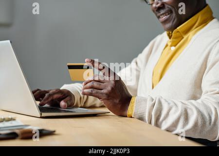 Close-up of African man sitting at table with laptop and using credit card for online payment Stock Photo