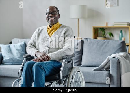 Portrait of African mature man with disability sitting in wheelchair in living room and laughing Stock Photo