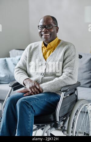 Portrait of African mature man with disability sitting in wheelchair and smiling at camera, he resting at home Stock Photo