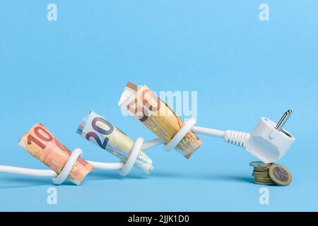 Euro bills tied in knots in electrical power cable with plug on coins stack on blue background. Concept of expensive electricity costs in Europe and r Stock Photo