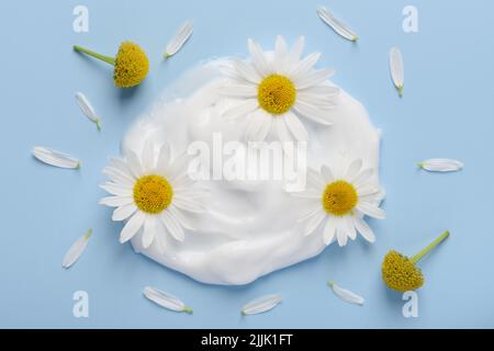White cosmetic cream with chamomile flowers and petals on blue background top view Stock Photo