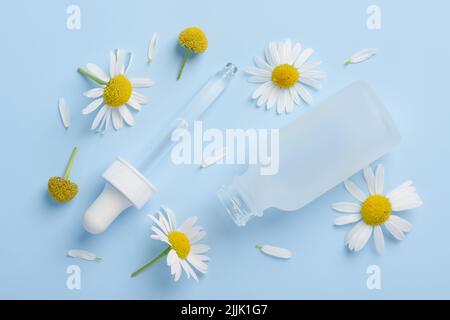 Cosmetic skincare serum dropper and bottle with chamomile flowers and petals on blue background top view Stock Photo