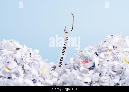 Word Data breach hooked on fishing hook pulled from pile of shredded documents on blue background Stock Photo