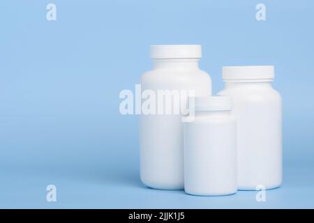 Three blank white plastic bottles of medicine pills or supplements on blue background with side copy-space Stock Photo