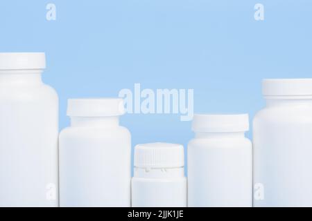 Row of blank white plastic bottles of medicine pills or supplements on blue background Stock Photo