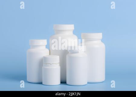 Different sizes of blank white plastic bottles of medicine pills or supplements on blue background Stock Photo