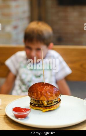 Happy girl, teenager eating a burger with a meat patty in a restaurant on a summer terrace. Food lifestyle. Fast food. Lunch Stock Photo