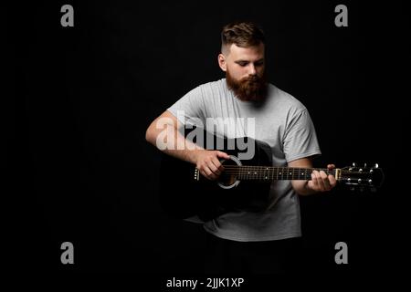 Portraite of handsome brunette bearded man musician, guitarist standing and holding a acoustic guitar in a hand. Stock Photo