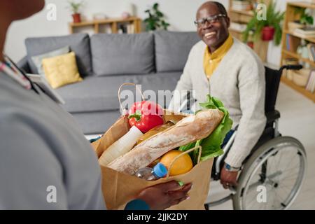 Close-up of caregiver holding paper bag with food bringing home for man with disability Stock Photo