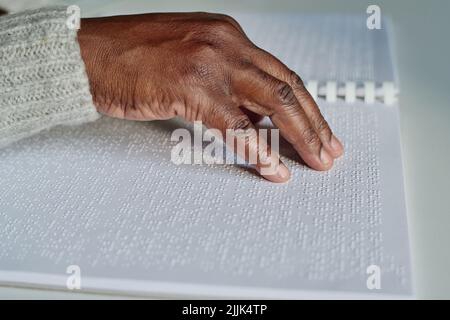 Close-up of African blind man reading with his right hand braille book at table Stock Photo
