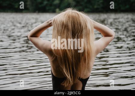 Young beautiful woman standing in the water and fixing her hair before swimming. warm summer evening. Stock Photo