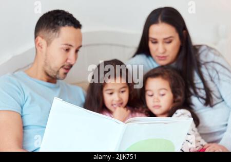 Nothing brings the family together like a good story. a man holding a storybook while sitting with his wife and two daughters. Stock Photo