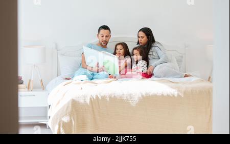 Each picture book is a world that children become a part of. a man holding a storybook while sitting with his wife and two daughters. Stock Photo