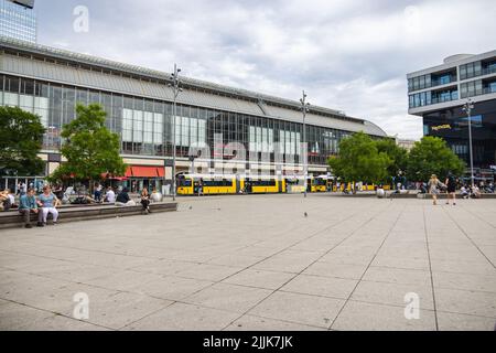 Berlin, Germany - June 29, 2022: View to the train station Alexanderplatz with a yellow tram on the station. people linger in the green areas of the s Stock Photo