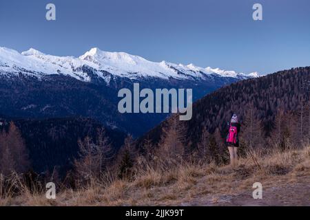 A hiker standing on the peak and admiring the snowy-peaked hill in front of her in spring Stock Photo