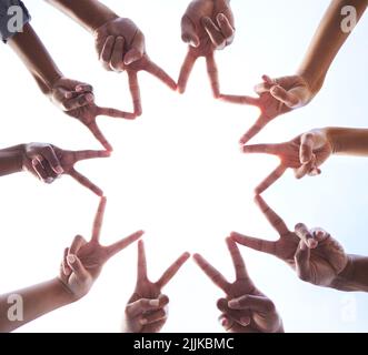 Positive energy gets the job done. Low angle shot of an unrecognisable group of businesspeople standing together and making a peace sign gesture. Stock Photo