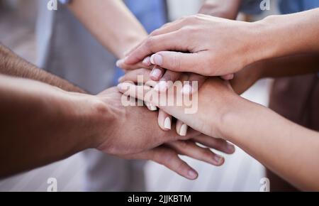 This is a team effort. an unrecognisable group of businesspeople standing together with their hands stacked in the middle. Stock Photo