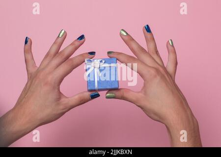 Female hands holding a small purple present box in a pink background Stock Photo