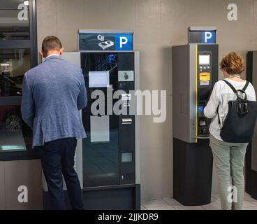 Unrecognizable Caucasian man and woman pay a parking ticket at a parking device in a parking garage in Haarlem, the Netherlands, Europe. Stock Photo