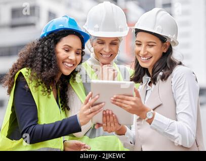 Plans are digital these days. three attractive female engineers using a tablet while working on a construction site. Stock Photo