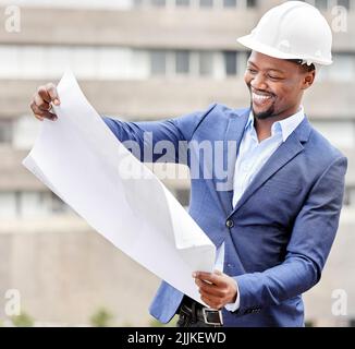 The man with the plan. a handsome young male engineer reading blueprints while working on a construction site. Stock Photo