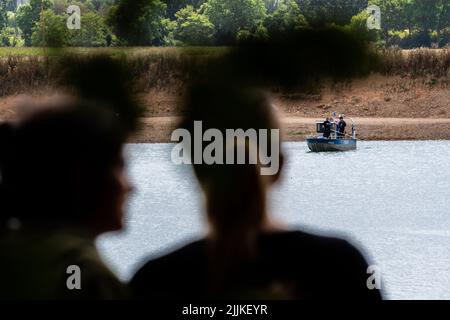 Porta Westfalica, Germany. 27th July, 2022. People look at a police boat sailing across the gravel pond where two people failed to surface for unexplained reasons while swimming on Sunday (24.07.2022). According to a spokesman for the fire department, some parts of the lake are about 30 meters deep. Experts from the police now want to search for the two people with an underwater probe. Credit: Lino Mirgeler/dpa/Alamy Live News Stock Photo